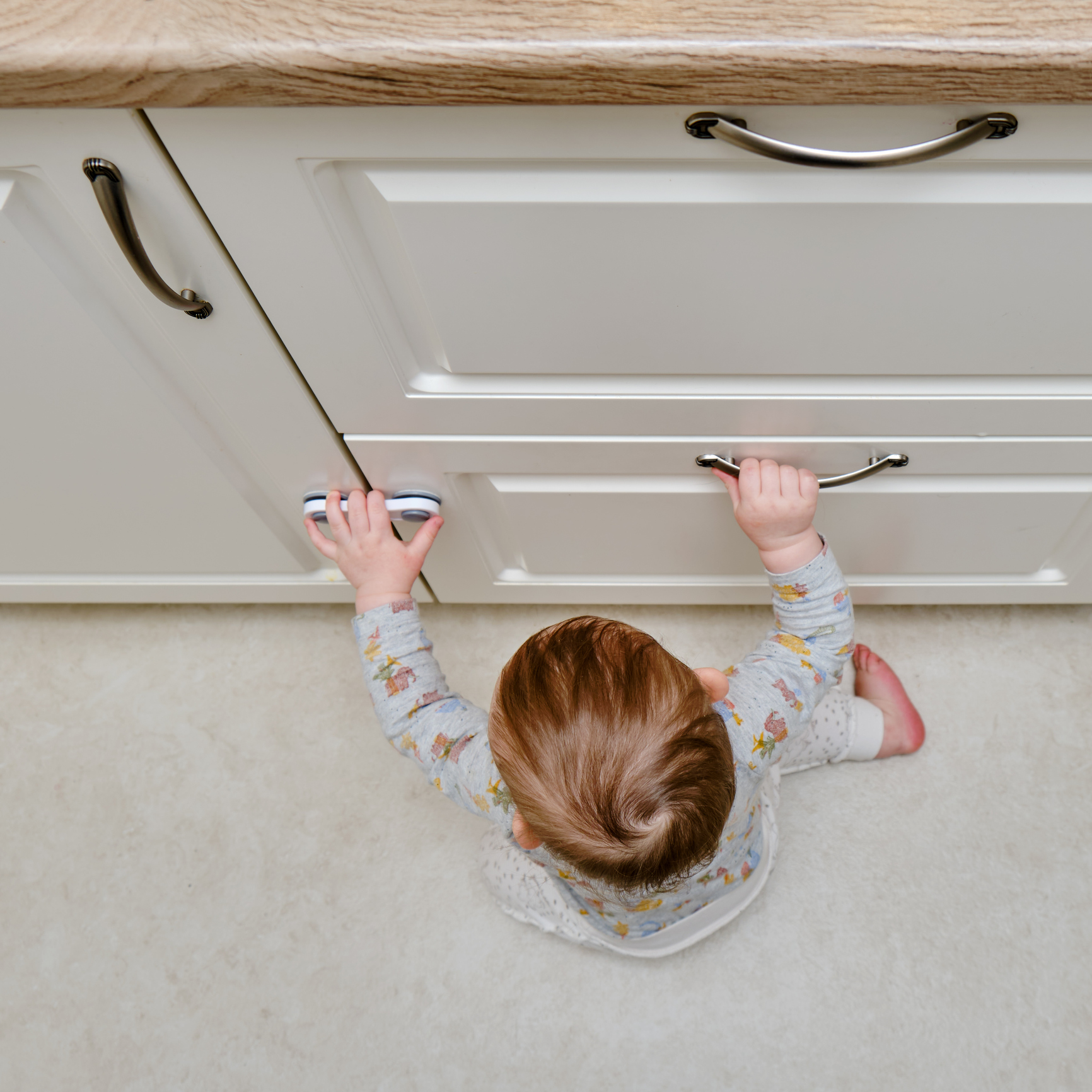 Toddler baby boy rips off a cabinet drawer with his hand. The child holds the cabinet door handle, small kid