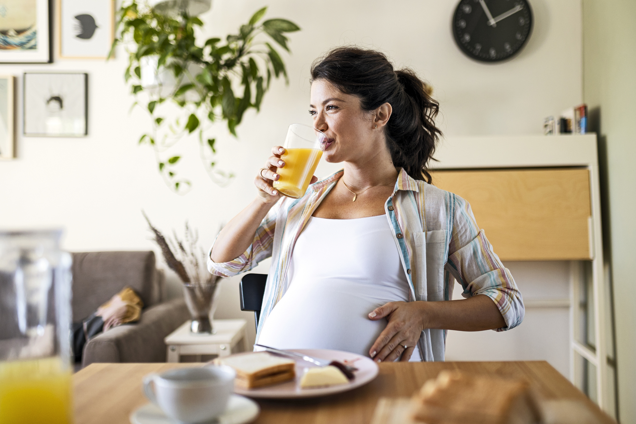 Young pregnant woman alone in her kitchen drinking juice after breakfast