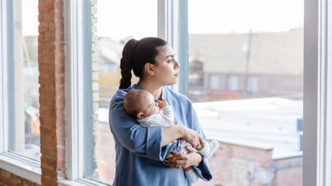 Mom looking out window while holding a baby