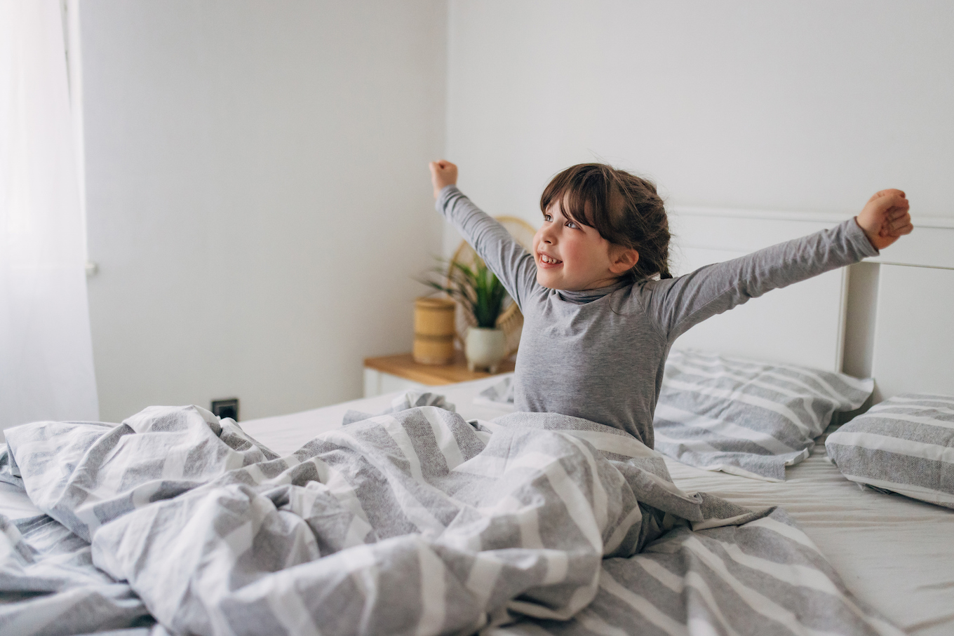 Awakening! Cheerful little girl stretches while sitting on her bed in the bedroom