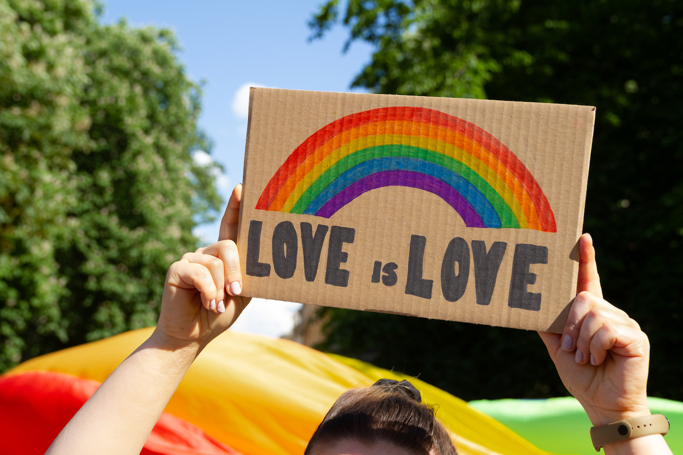 Woman holding placard sign Love is Love with rainbow, symbol of LGBT community. Pride Parade, gay lesbian equality march.