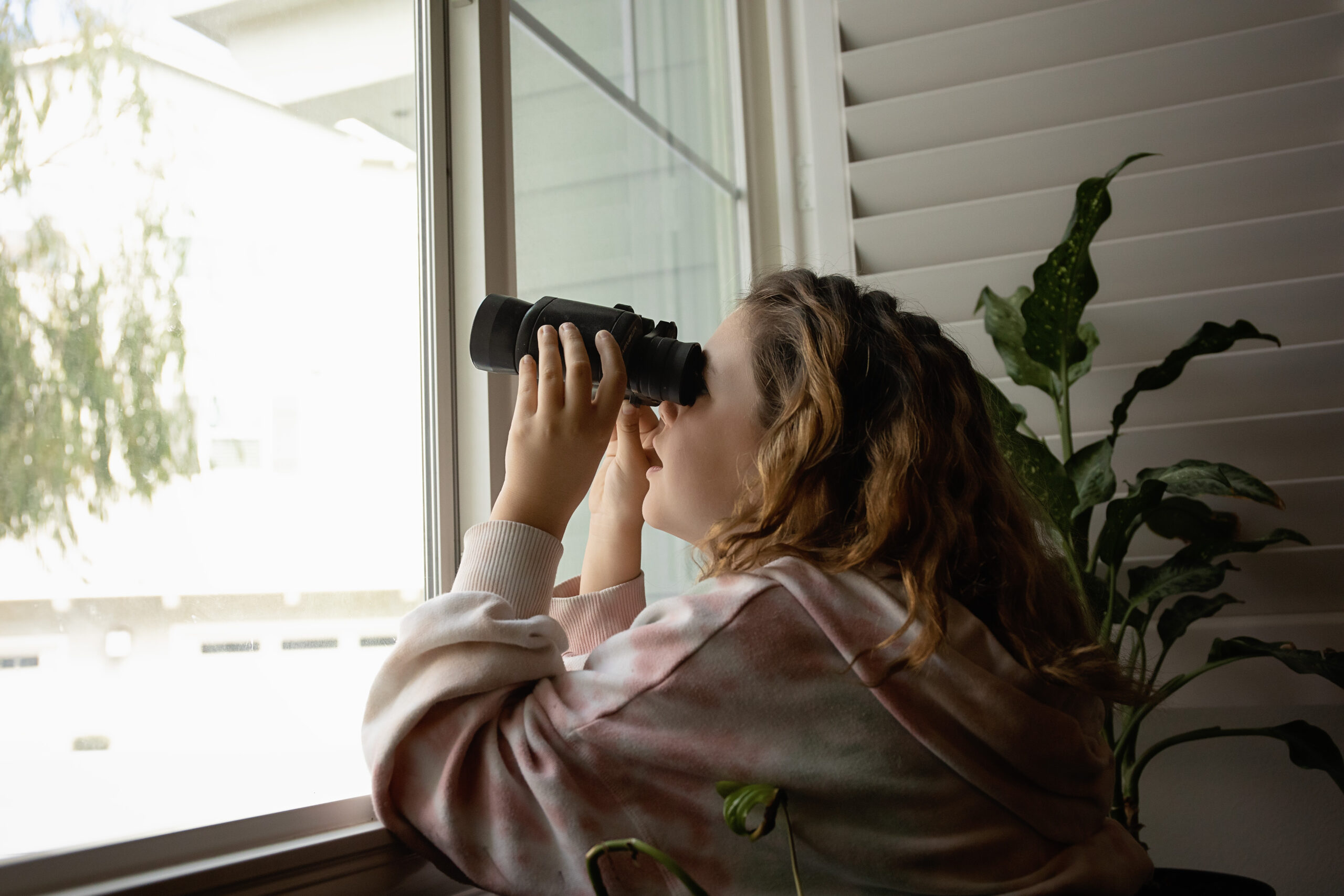 Girl looking out window with binoculars