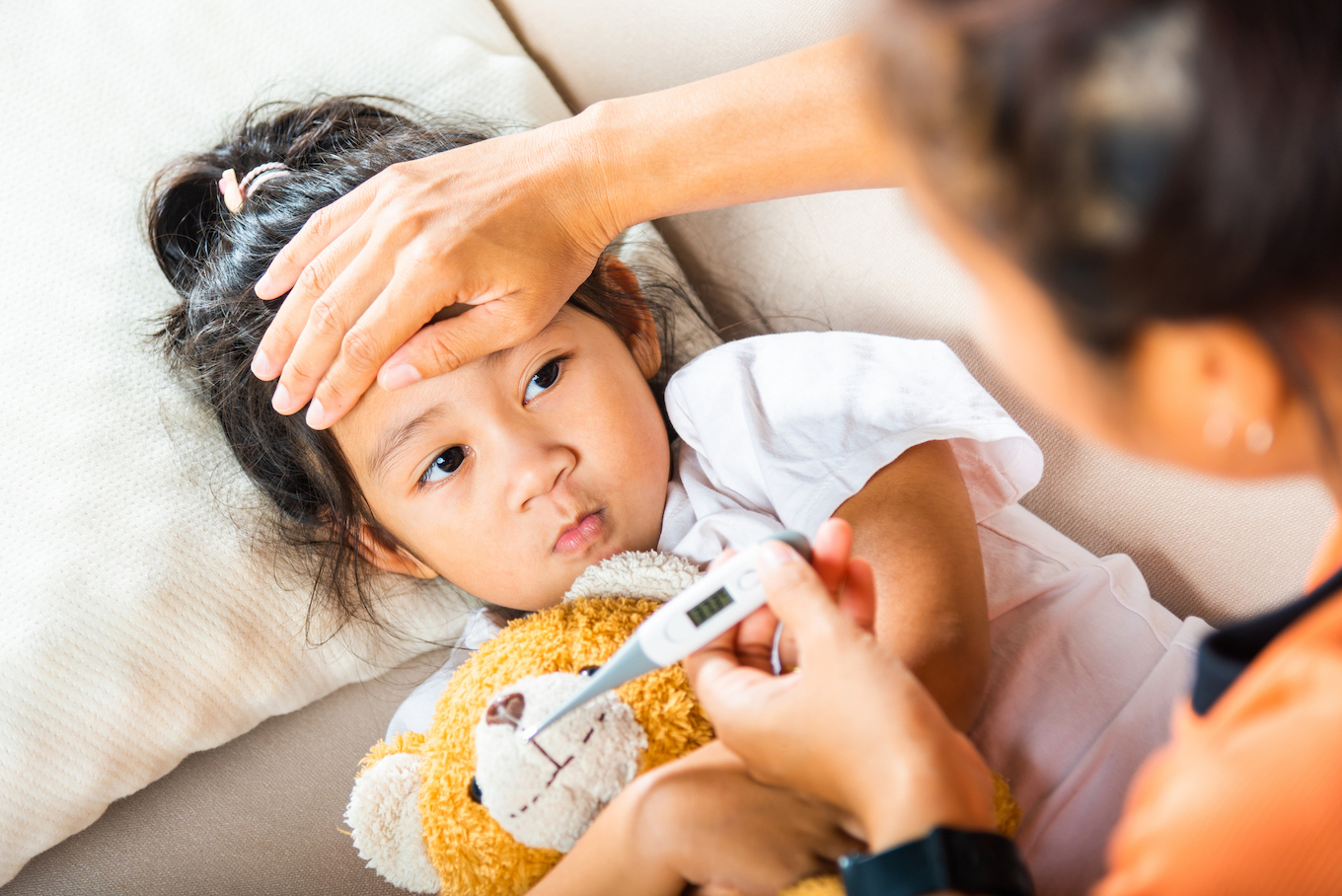 Mother checking temperature of her sick daughter with thermometer in mouth