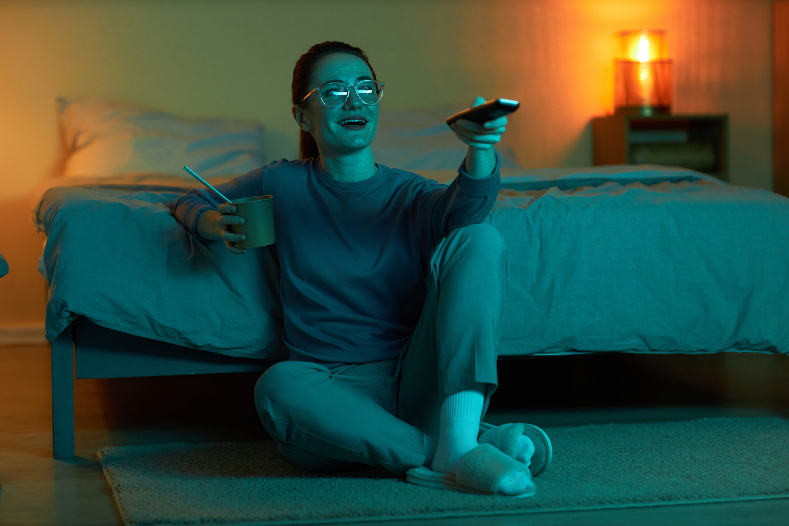 Smiling woman watching TV at home holding remote control