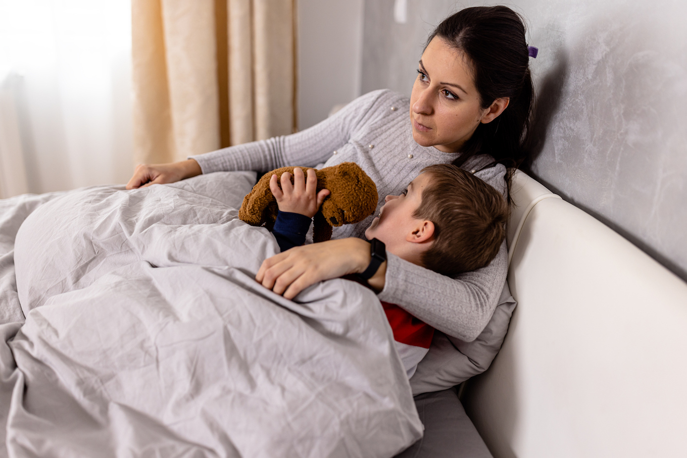 A happy kid is enjoying time with his mother in bed.