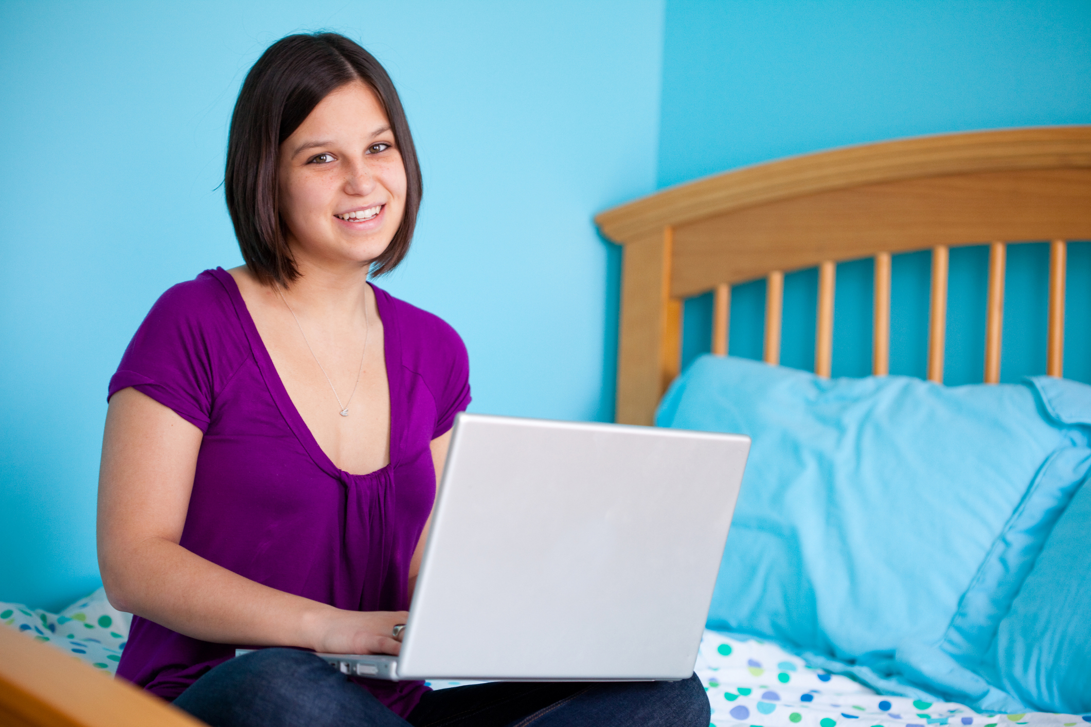 Smiling teen working with laptop on her bed