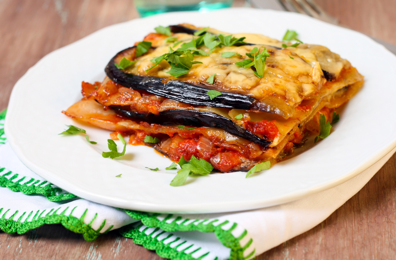 Slice of vegetable lasagna on a white plate on wooden table
