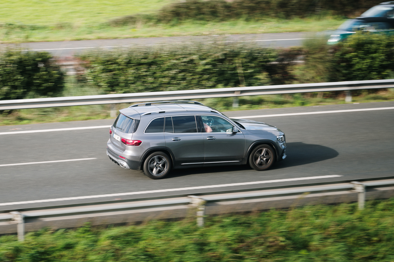 a gray SUV down the highway with green bushes on either side