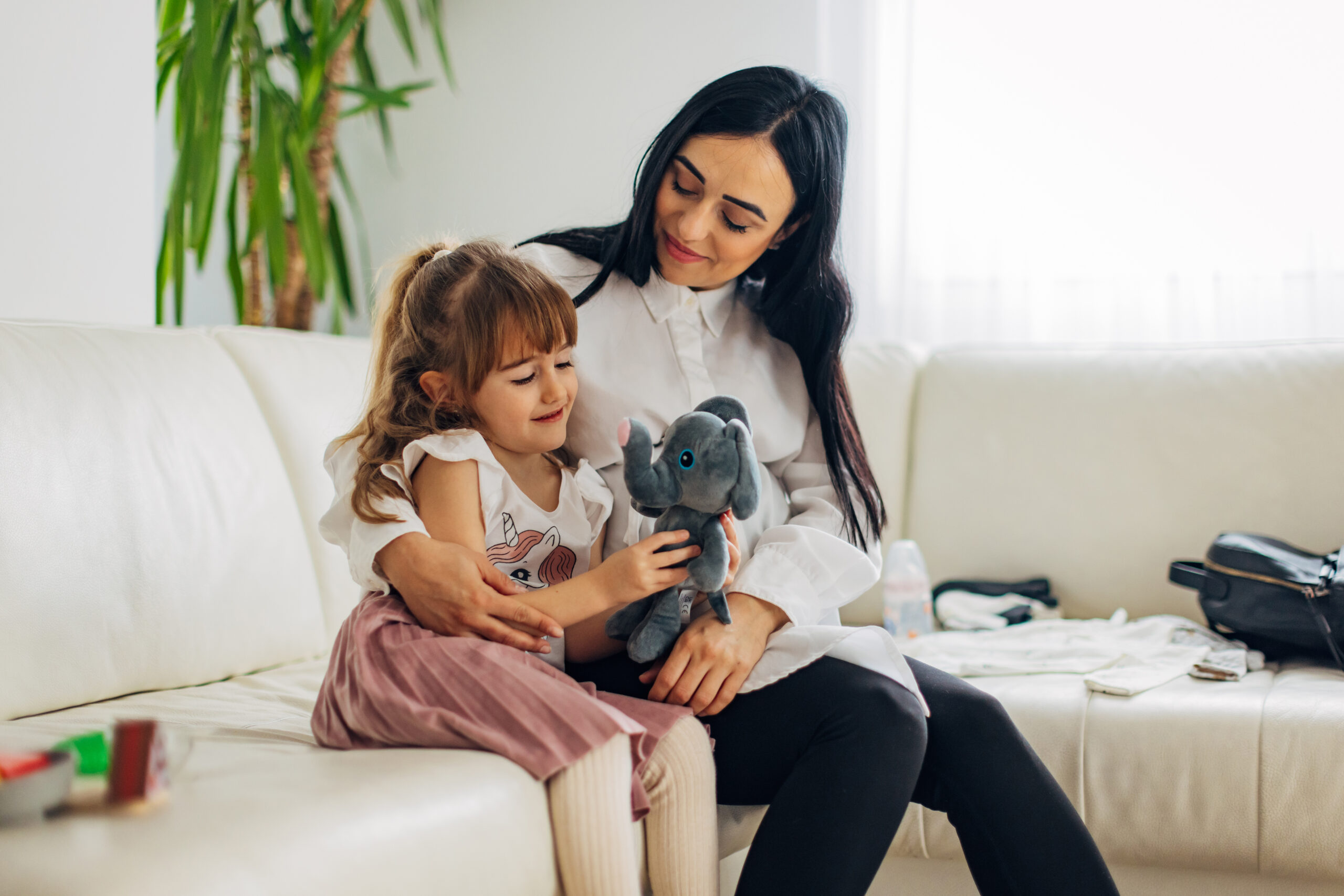 A smiling mother hugs her daughter who is playing with her stuffed toy elephant