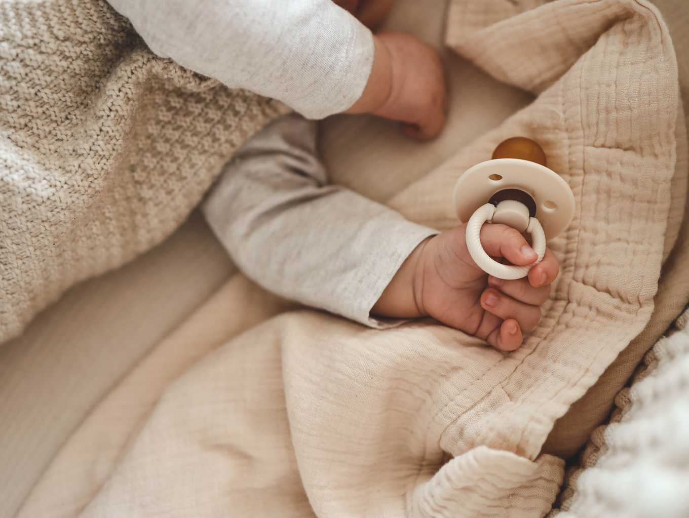 Baby with a nipple. Close up of baby hands with pacifier. Focus is on hands. Newborn sleeping on a blanket holding a pacifier in his hand