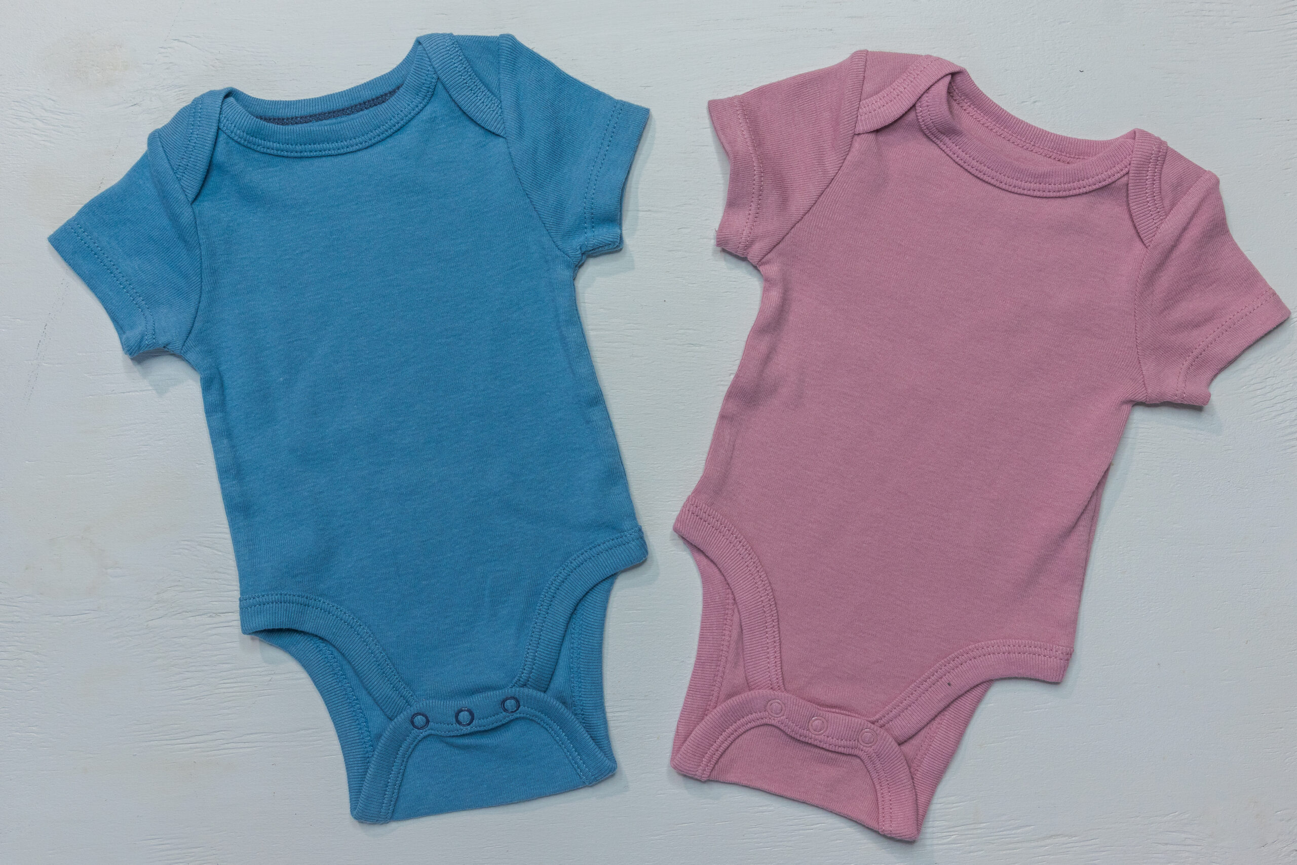 Flat lay of two onesies on white background for gender reveal or baby announcement
