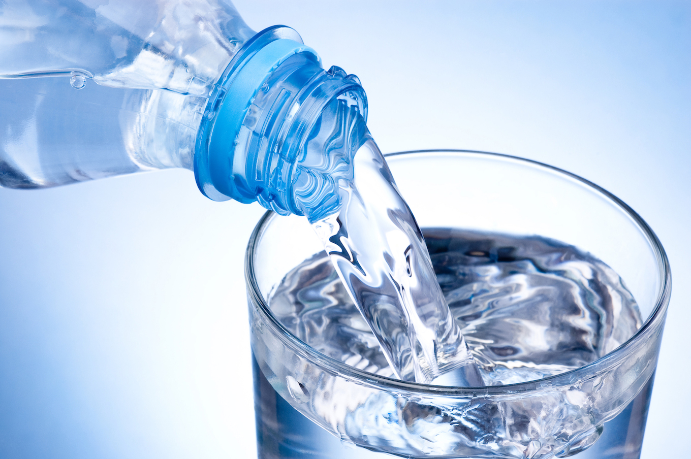 Pouring glass of water from plastic bottle on blue background