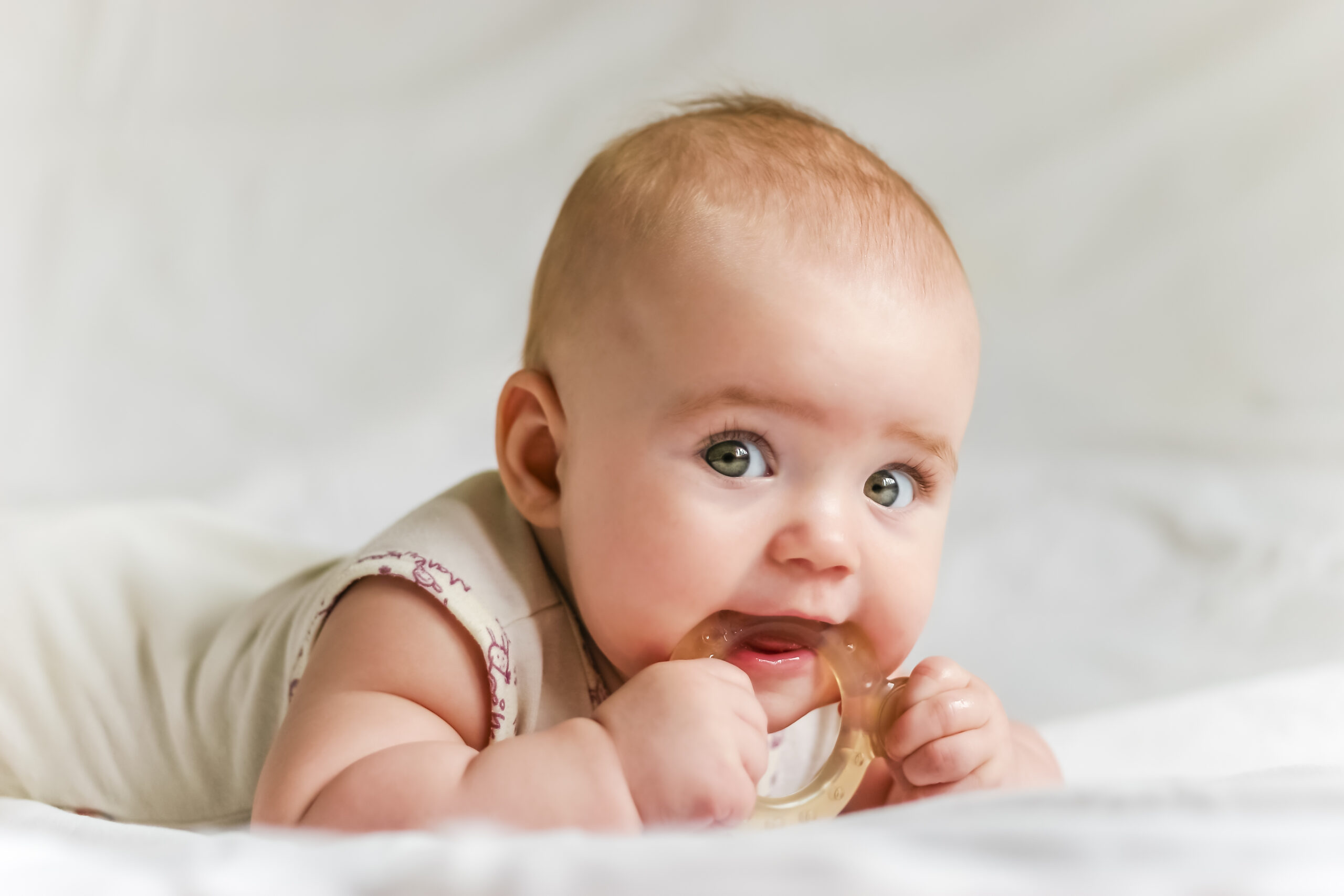 Baby girl on her stomach with teether in the mouth