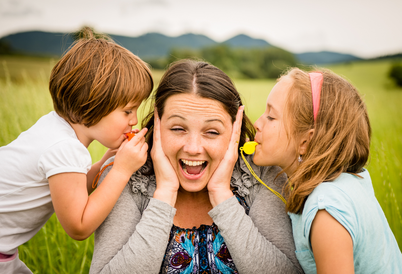 Children blowing whistle to mother's ears