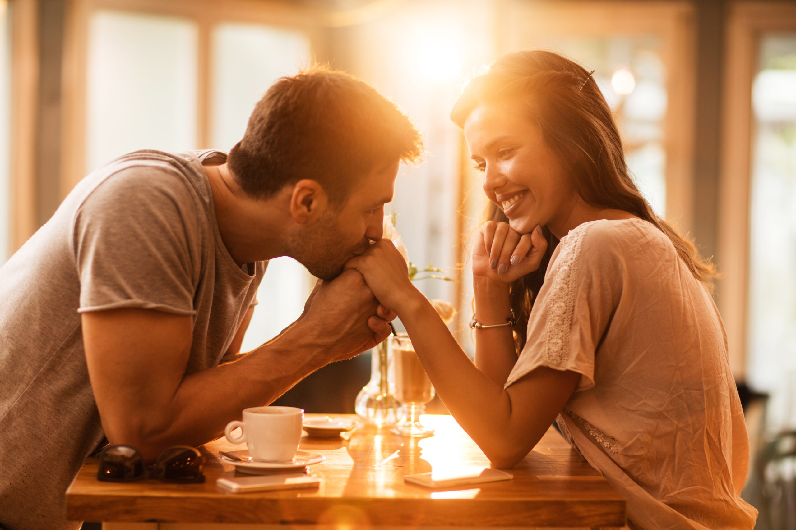 Young romantic man kissing girlfriend's hand in a cafe.