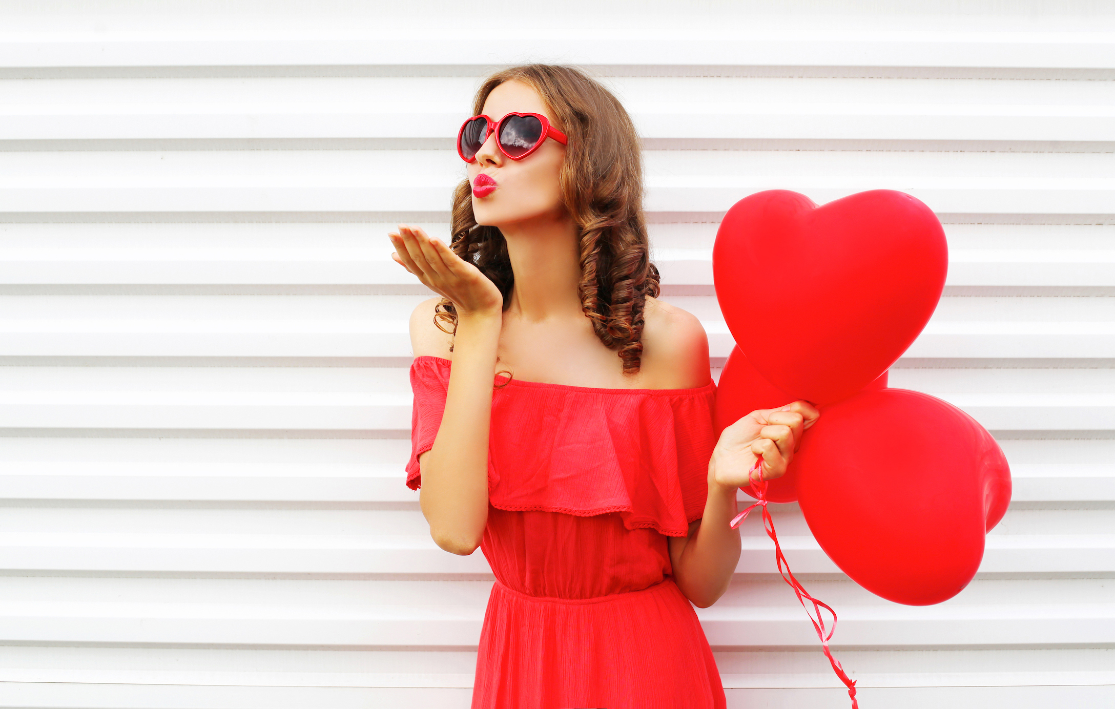 woman blowing kisses and holding heart-shaped balloons