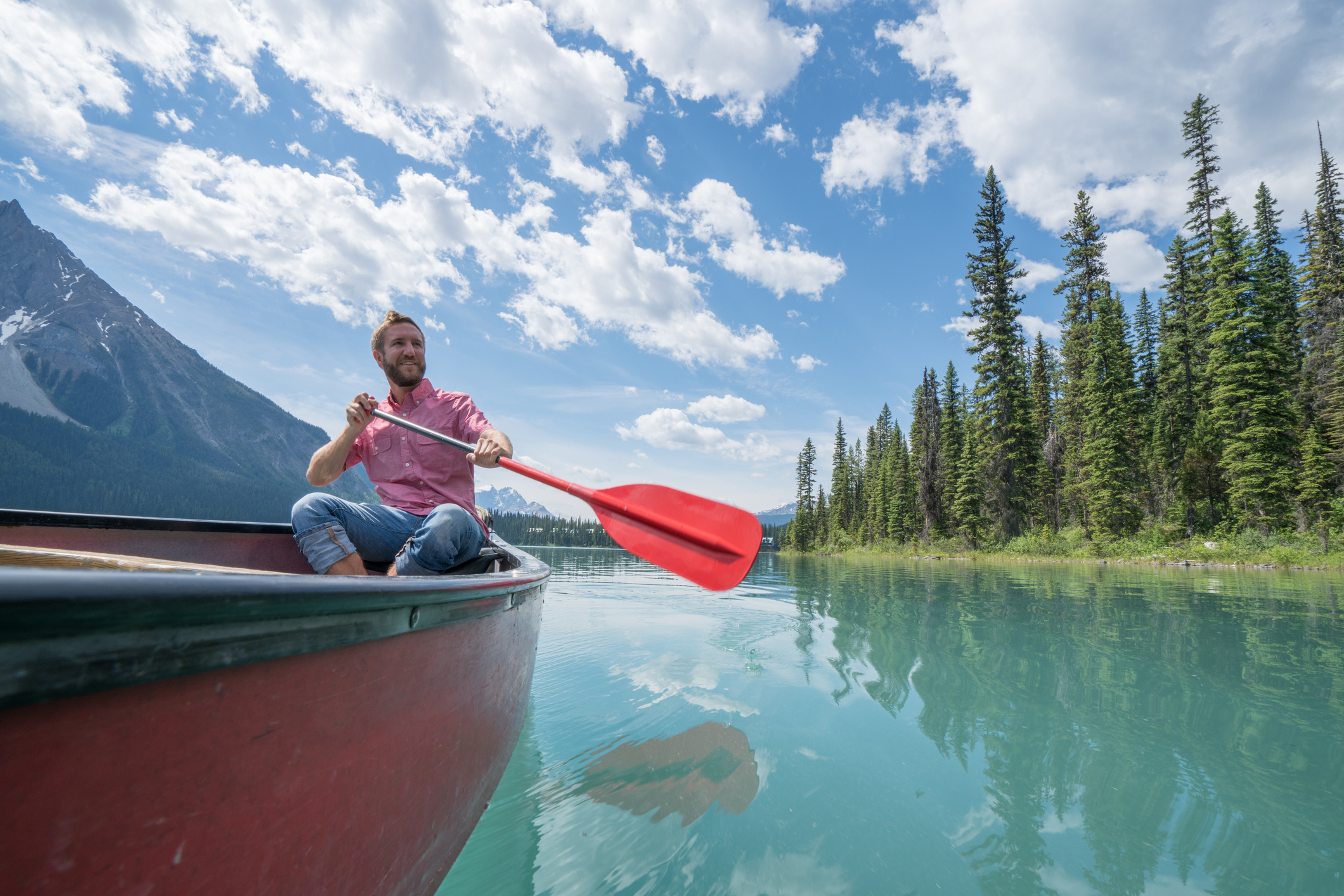 Young man paddling red canoe on turquoise lake