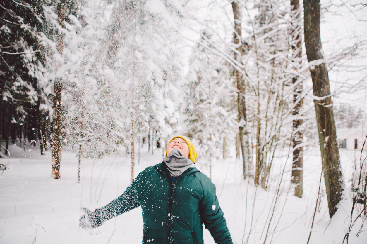 A boy is throwing snow in the air and enjoying it on his face.
