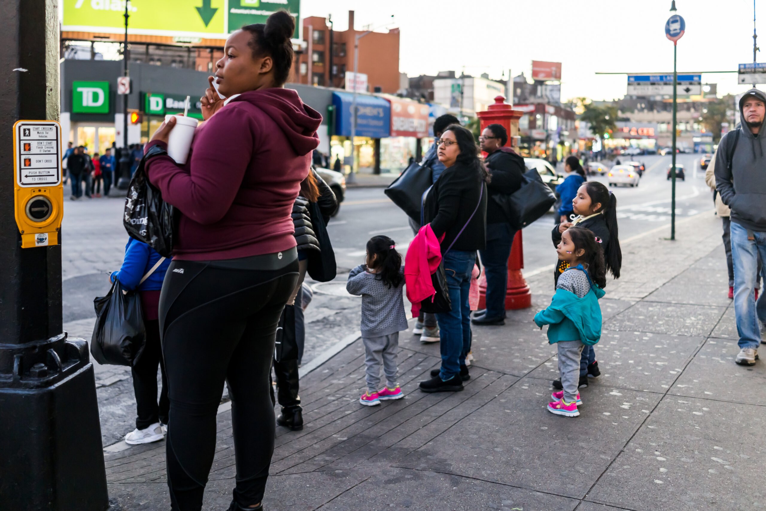 People family waiting to cross street in Fordham Heights center, New York City, NYC in evening