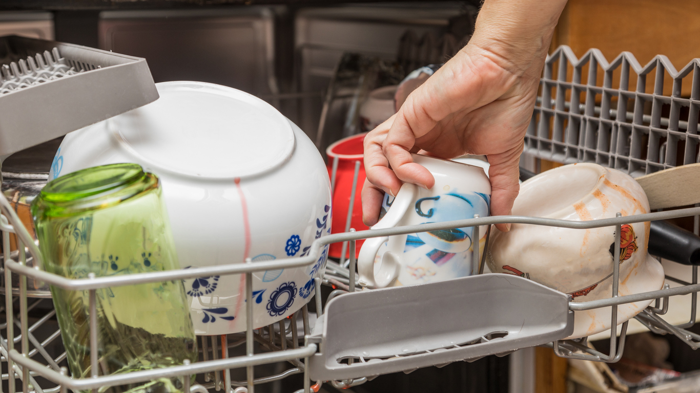 One hand loads a dishwasher