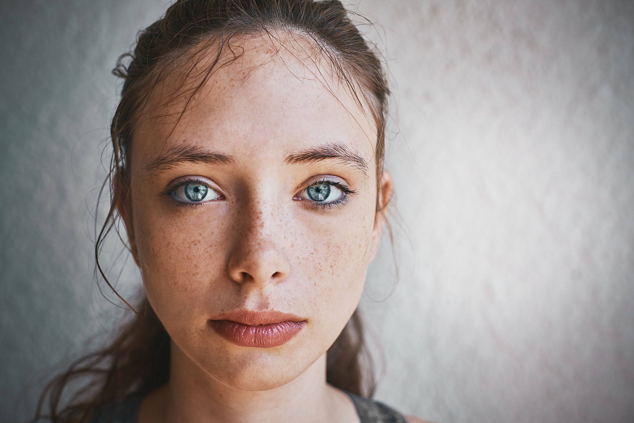 Beautiful blue-eyed brunette standing by textured wall looks sad