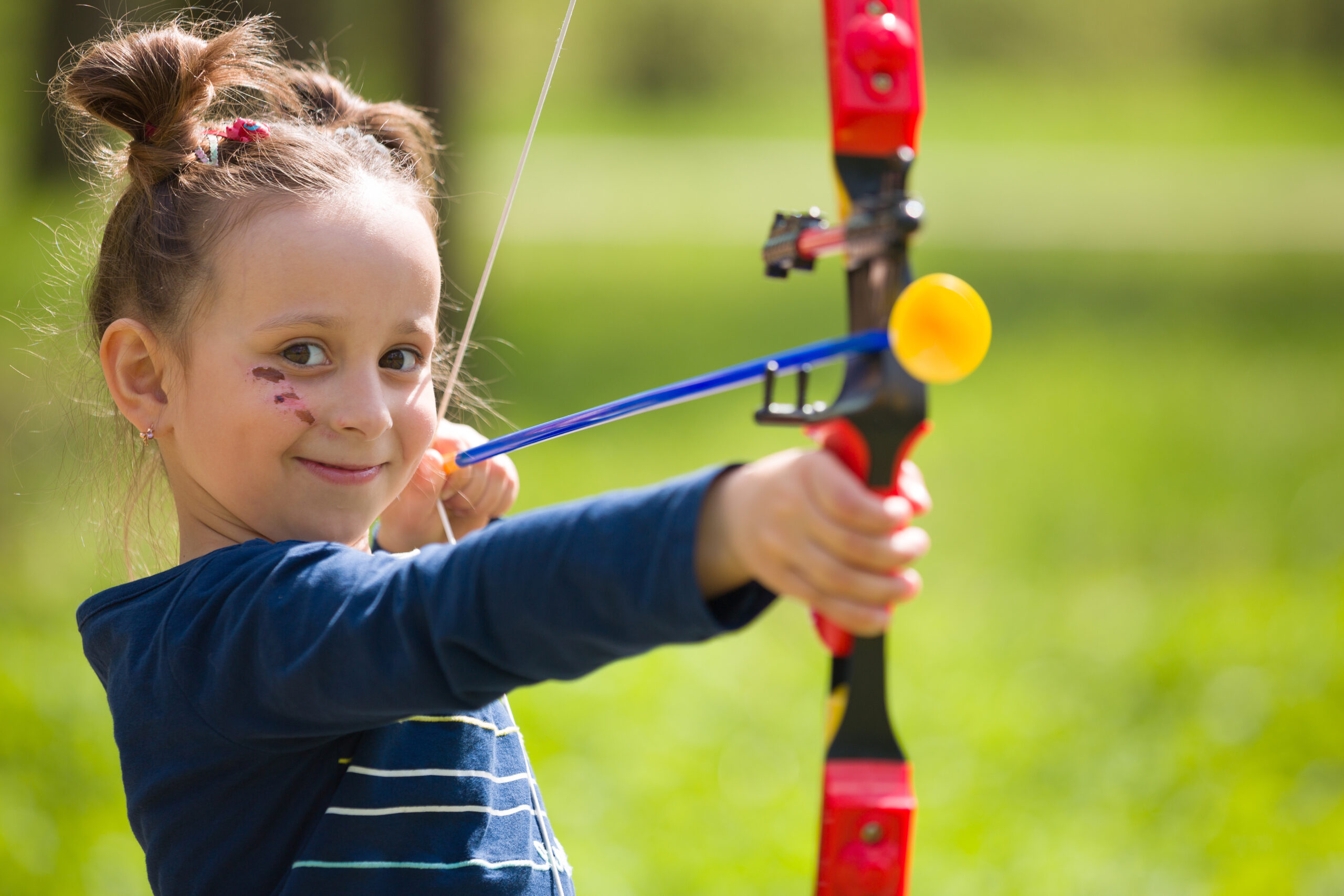 Cute girl archer with bow shooting in sunny summer day. little girl shoots bow in the park. Outdoors. Sport activities with children. Sport and lifestyle concept. Aiming high Cute girl archer with bow shooting in sunny summer day. little girl shoots bow in the park. Outdoors. Sport activities with children. Sport and lifestyle concept. Aiming high