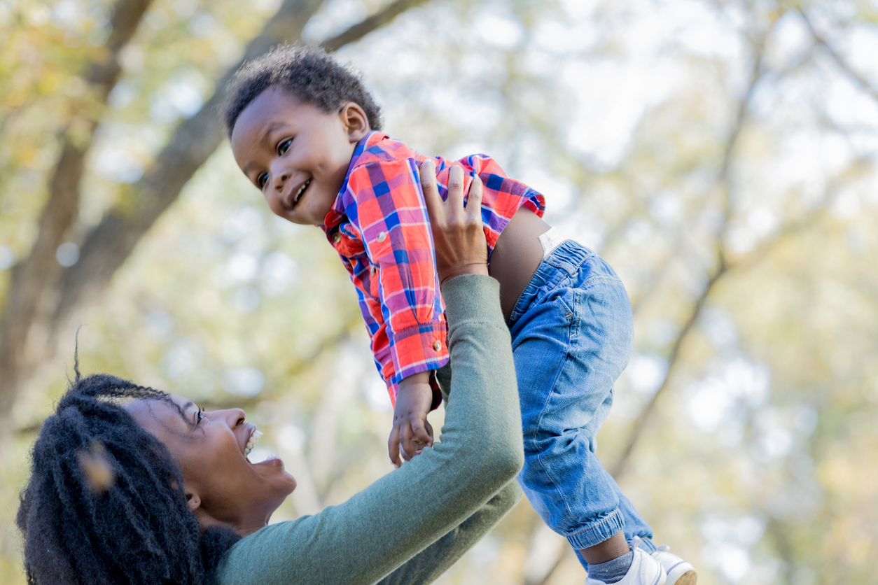 Playful mother holds baby boy in the air outside