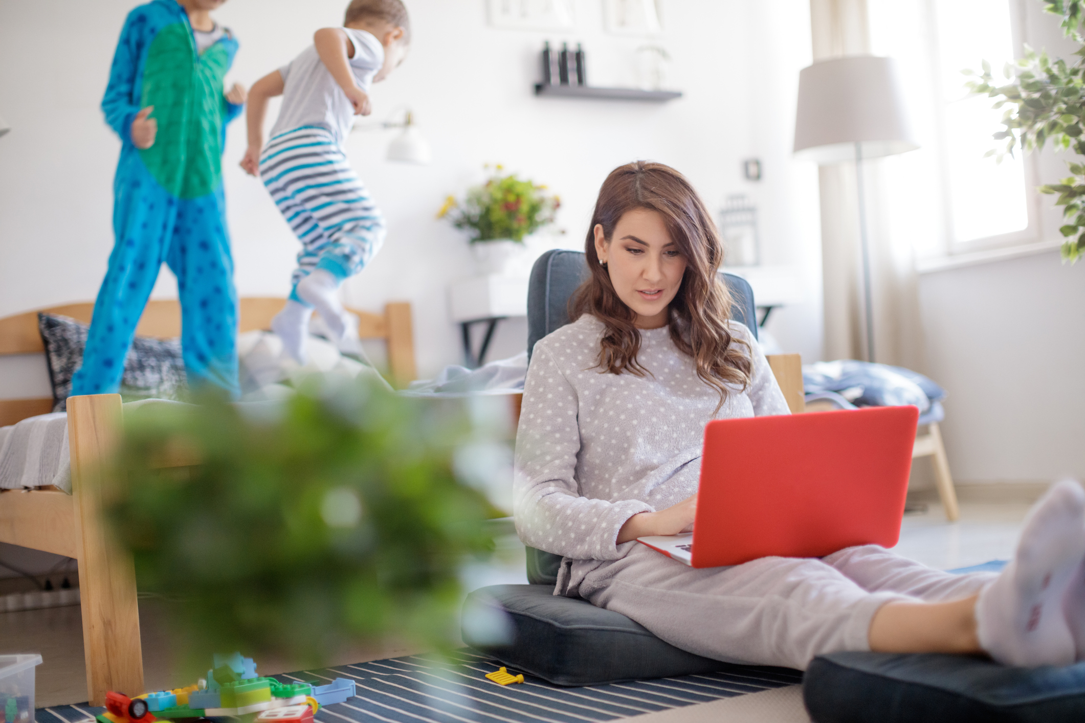 Mother working at home on laptop, sons jumping on the bed