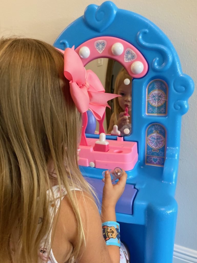 Little girl putting on pretend lipstick in mirror