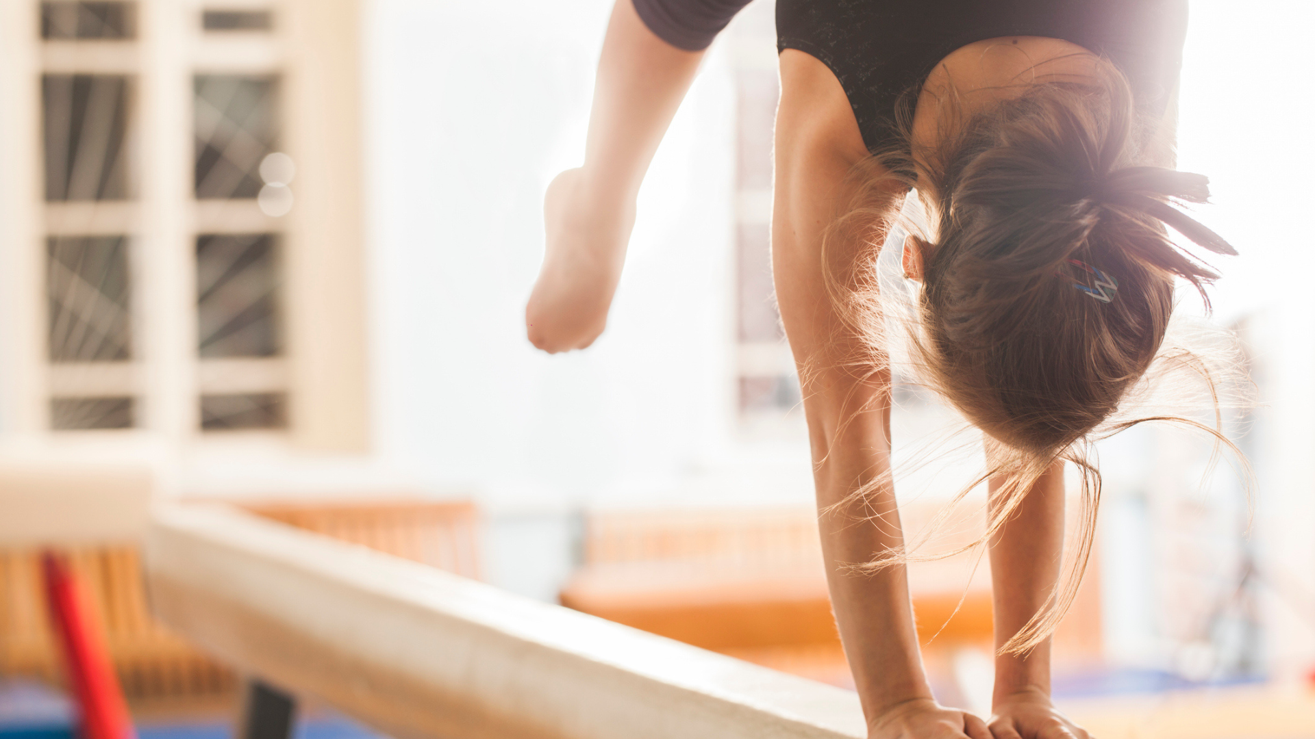 a teen girl in a handstand on a balance beam