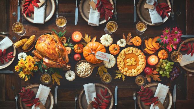 Thanksgiving celebration traditional dinner. Roasted turkey garnished with cranberries on a rustic style table decoraded with pumpkins, vegetables, pie, flowers and candles. Festive table setting