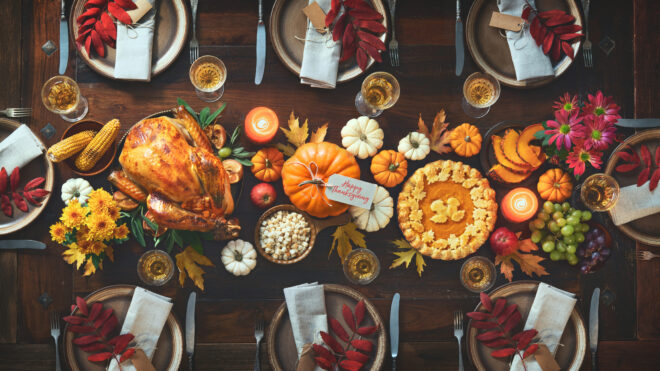 Thanksgiving celebration traditional dinner. Roasted turkey garnished with cranberries on a rustic style table decoraded with pumpkins, vegetables, pie, flowers and candles. Festive table setting