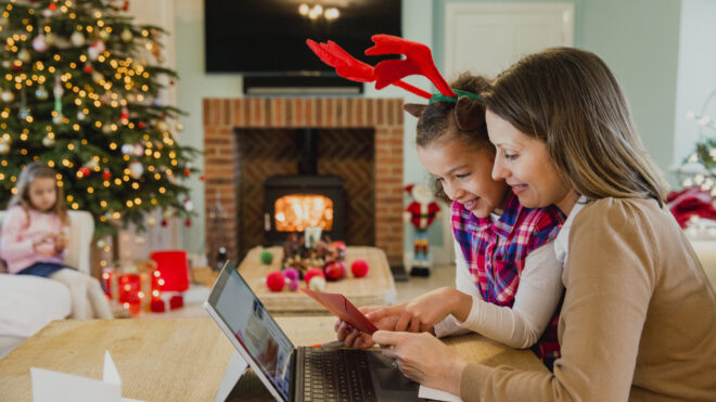 Little girl making and writing out christmas cards with her mother at the dining table in their home.