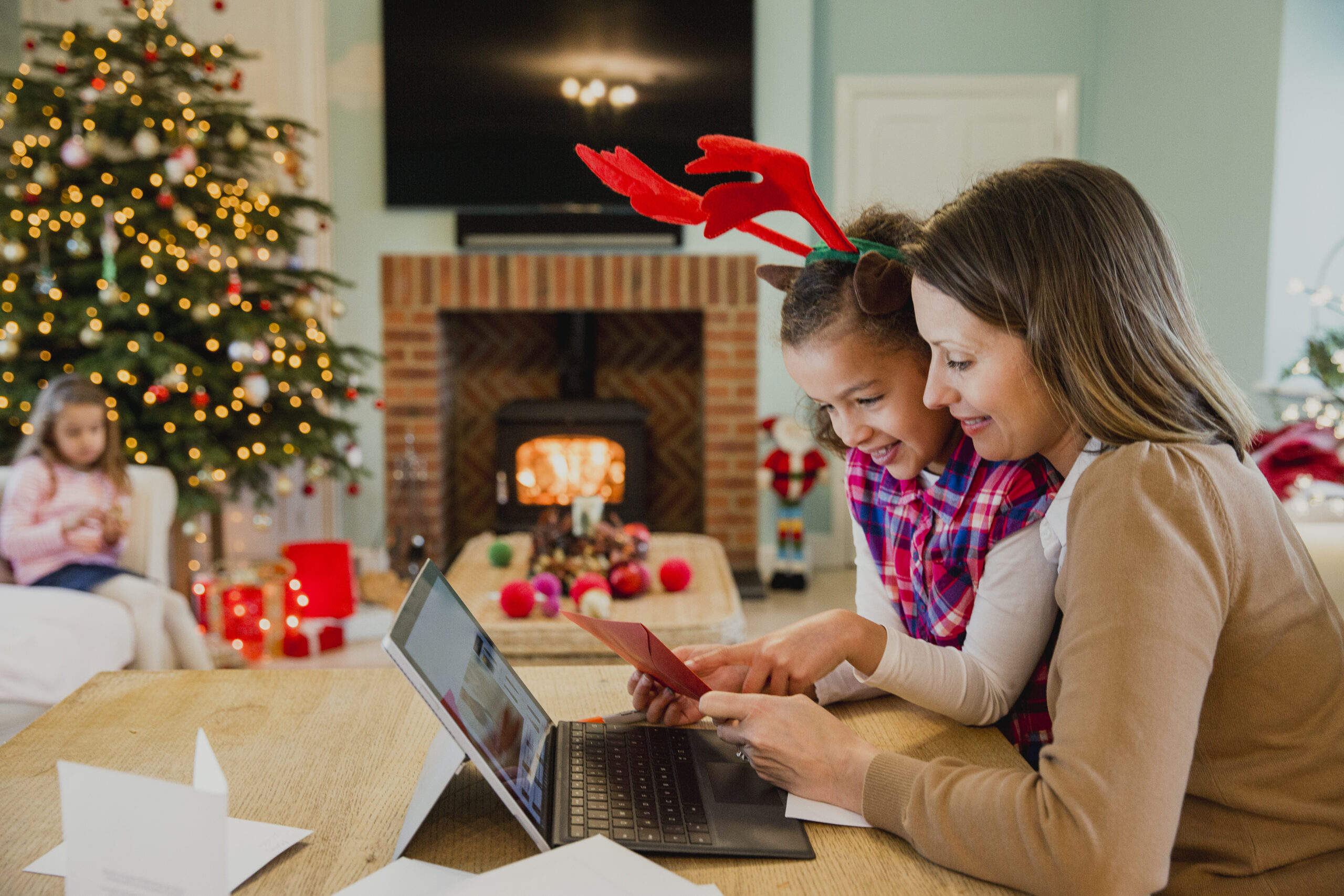 Little girl making and writing out christmas cards with her mother at the dining table in their home.