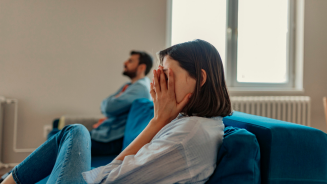 woman close-up with her hands covering her face while man sits in the distance