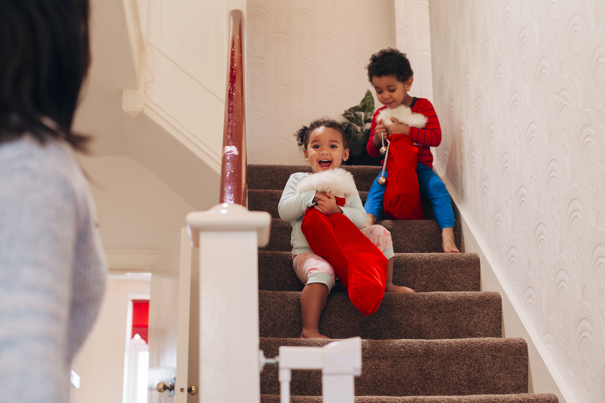 Brother and sister coming down the stairs on Christmas morning, carrying their stockings about to go see what is left under the tree for them.