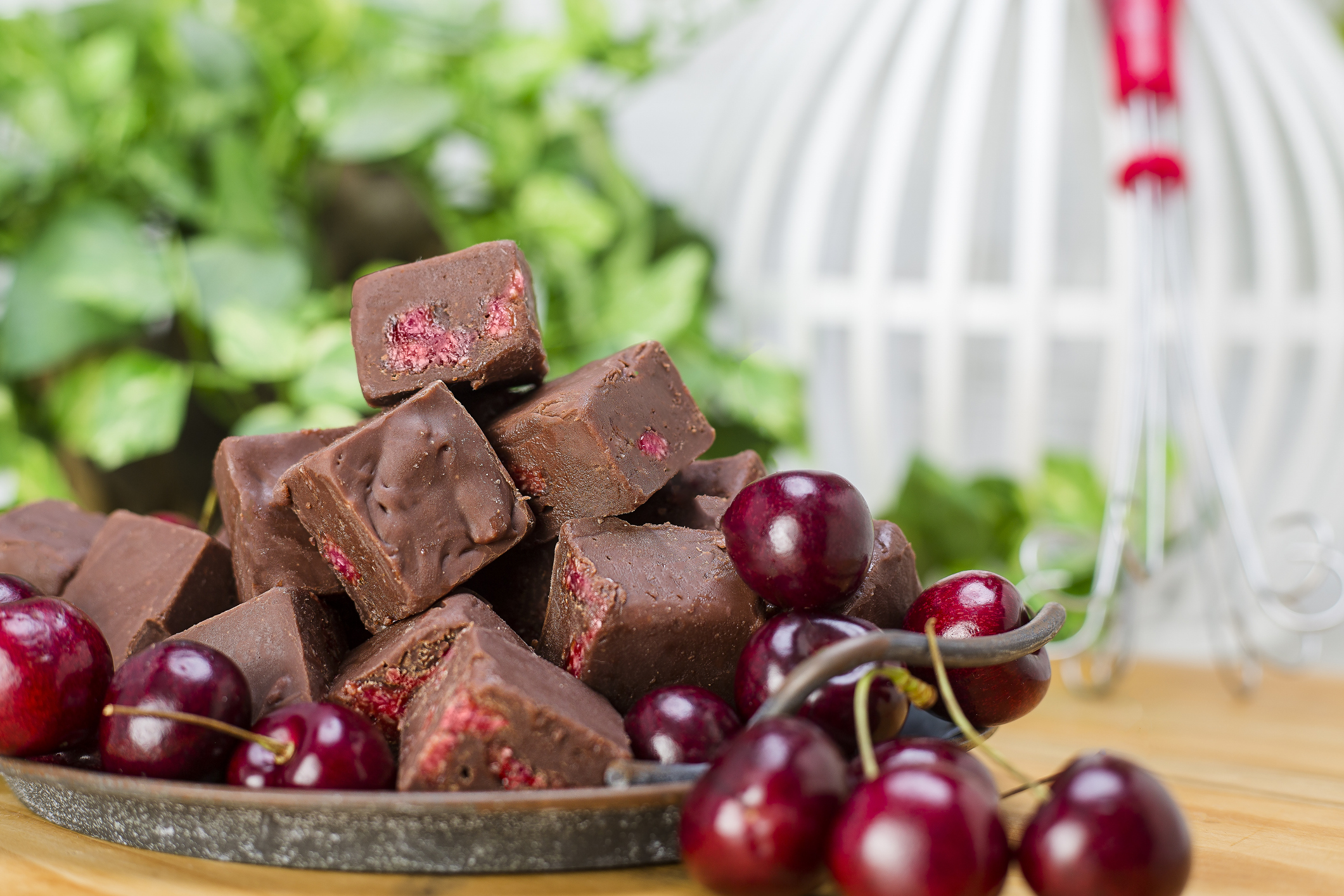 Cherry and chocolate fudge on a metal tray surrounded by cherries. Front view of cherry and chocolate fudge with cherries on a vintage metal tray.