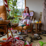A teenager with vibrant dyed red hair with her grandmother in their living room in their home in Hexham, Northumberland in the North East of England. She is looking and smiling at the camera as she holds a new diary and pencil case which she has been gifted for Christmas.