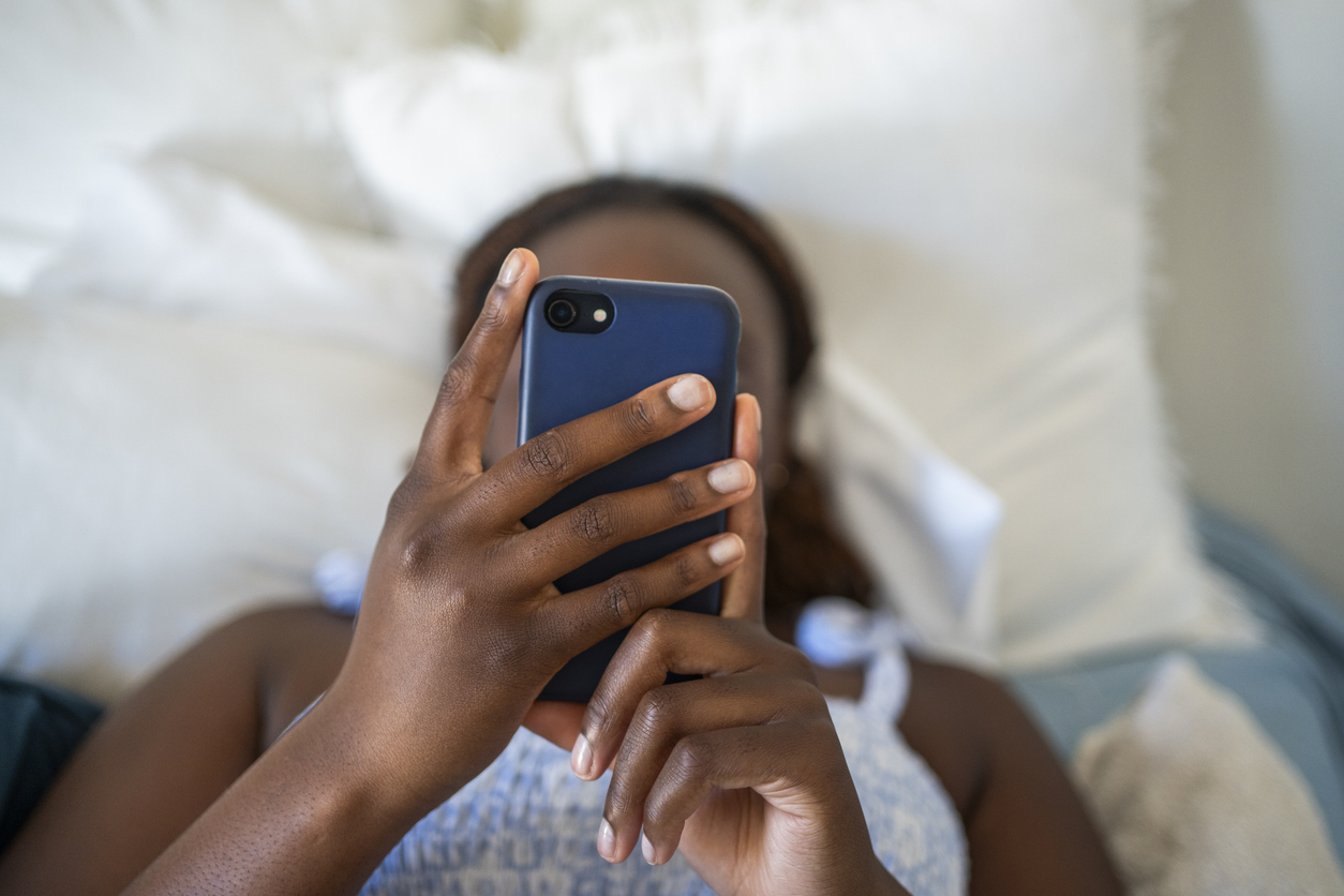 Teenage girl using a phone while lying on her bed Teenage girl using a phone while lying on her bed