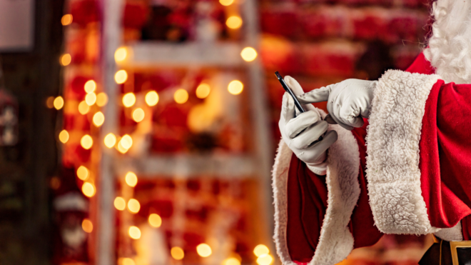 Santa Claus hands scrolling on the phone with a house behind him