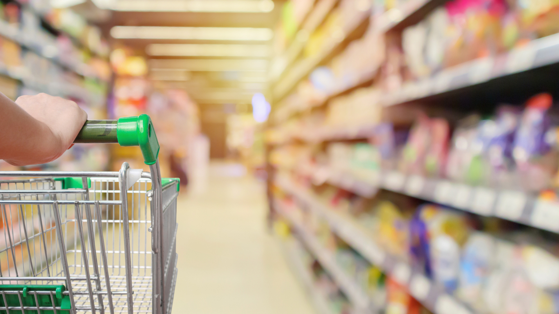 grocery store shopper person's hand seen pushing shopping cart in supermarket aisle with blurred product shelves