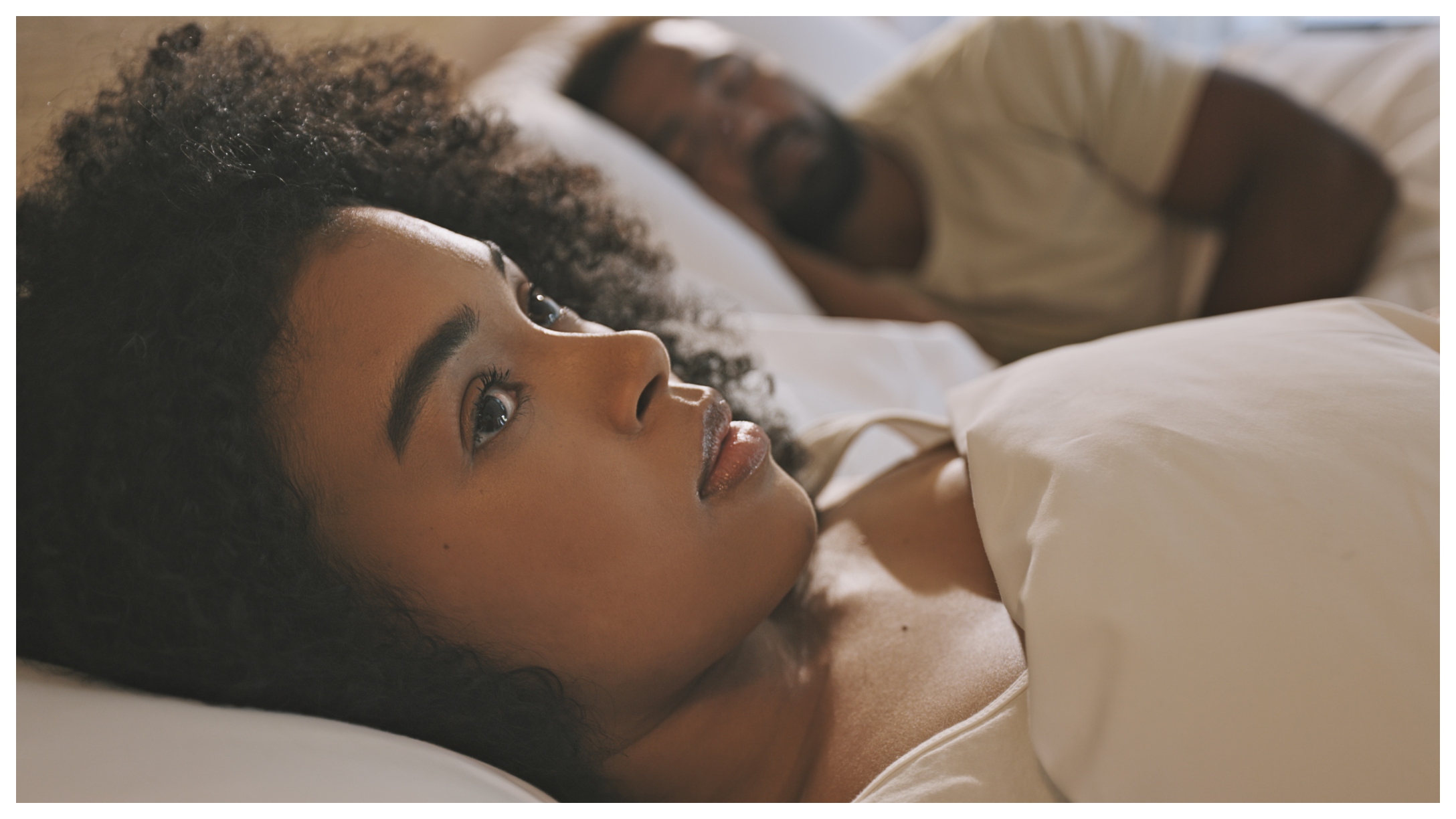 Black woman awake in bed with man asleep next to her