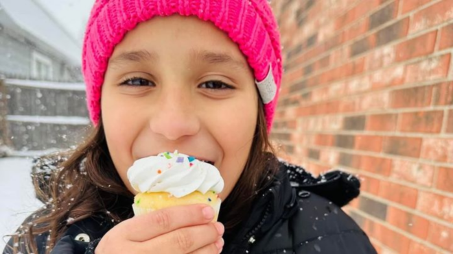 Serenity Campos, a young girl in a bright pink beanie eating a sprinkled cupcake