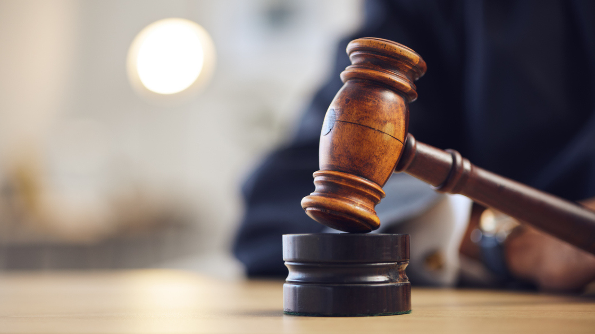 a man sitting at a table in a courtroom in the background. a gavel in the foreground