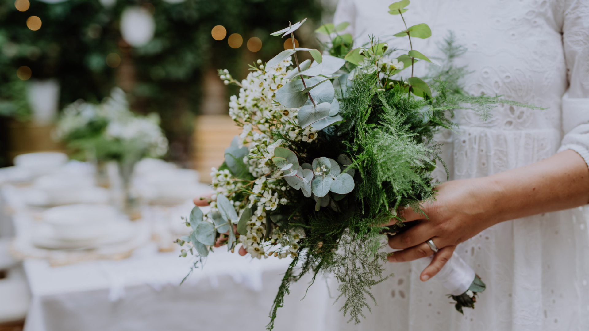 a bride in a white dress holding an elaborate bouquet of flowers with an empty table in the background