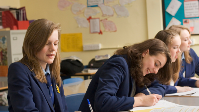 four girls sitting at a desk wearing school uniforms
