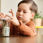 Child saving money in a glass jar at home