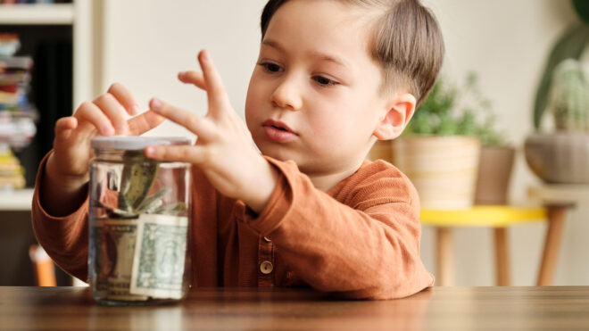 Child saving money in a glass jar at home