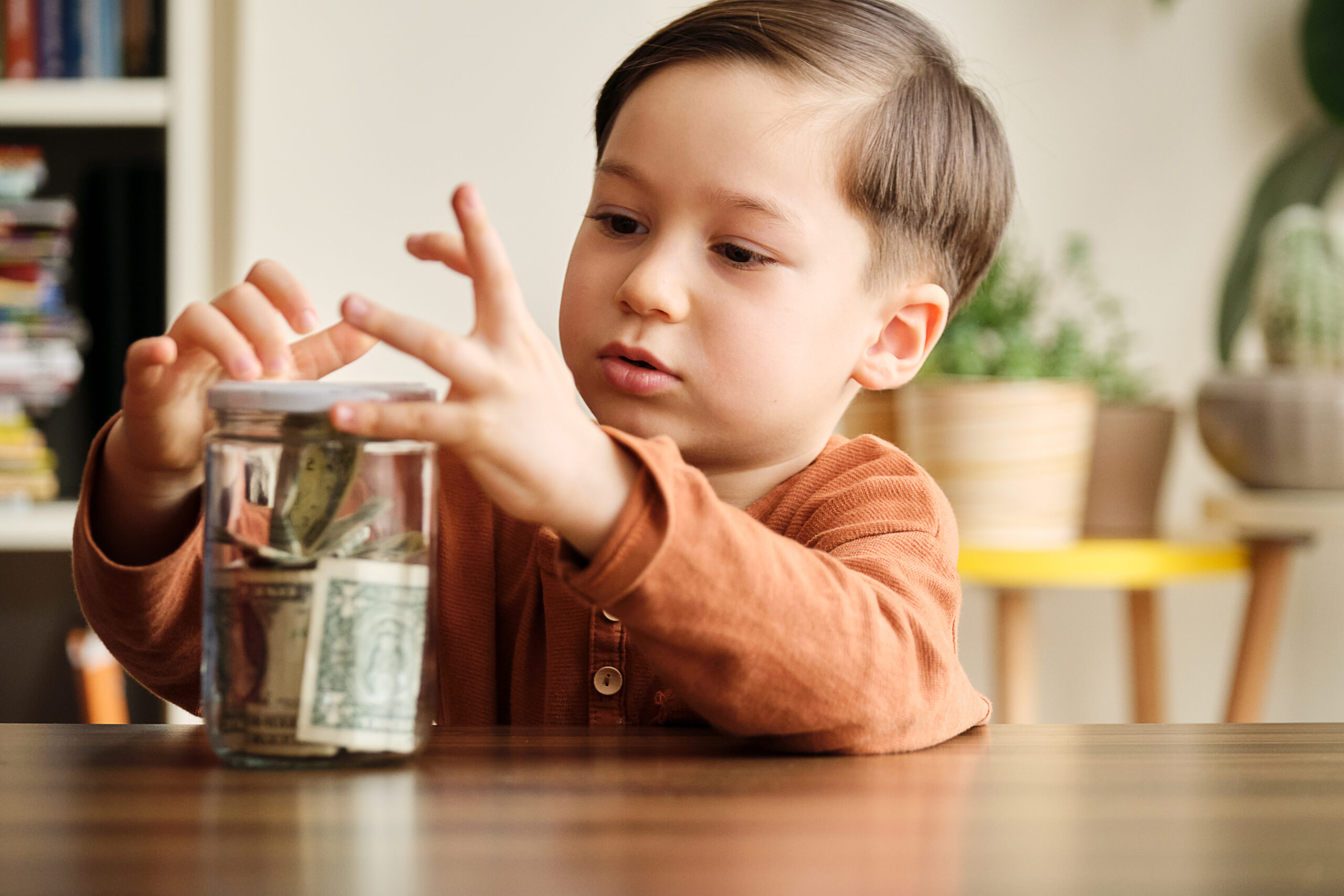 Child saving money in a glass jar at home