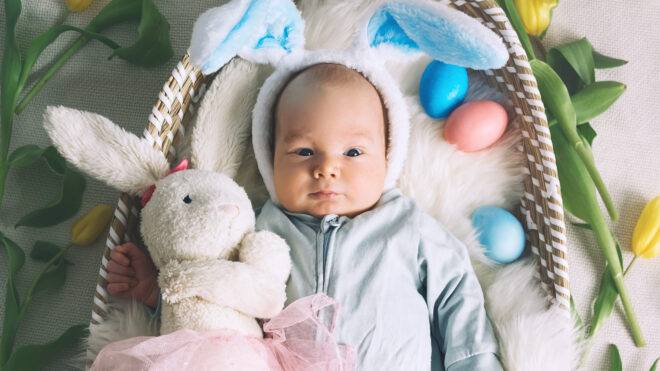 Cute baby Easter bunny. Little baby boy with bunny ears and Easter eggs in wicker basket in white fur. Symbol of Easter holiday, birth, spring, religion.